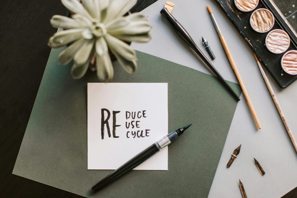 Flat lay of art materials featuring a recycle-themed note and calligraphy tools.