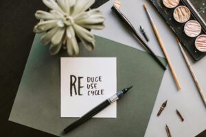 Flat lay of art materials featuring a recycle-themed note and calligraphy tools.
